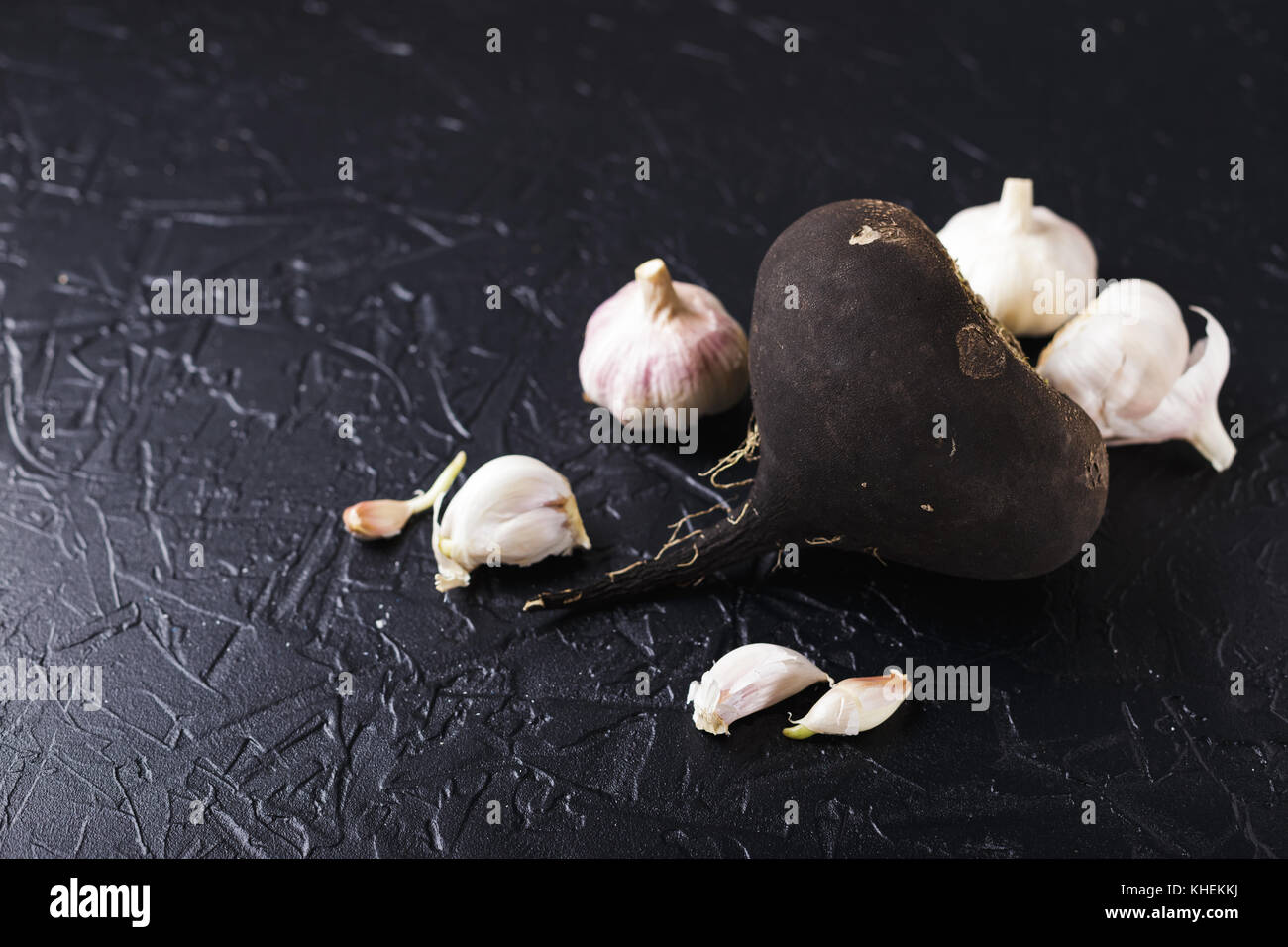 Il tubero Rafano nero e aglio su un nero lo sfondo di calcestruzzo Foto Stock