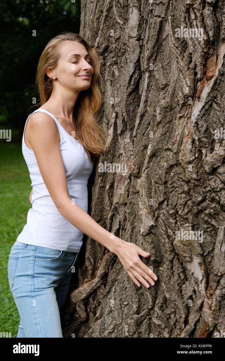 Giovane donna abbracciando grande albero Foto Stock