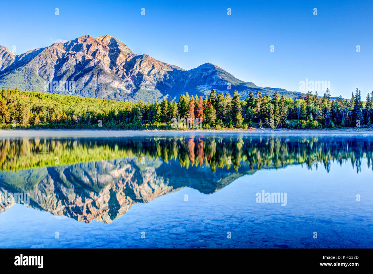 Alberi colorati rivestiti sulle rive del lago di patricia al parco nazionale di Jasper con montagna piramidale in background. Il lago calmo riflette uno specchio imag Foto Stock