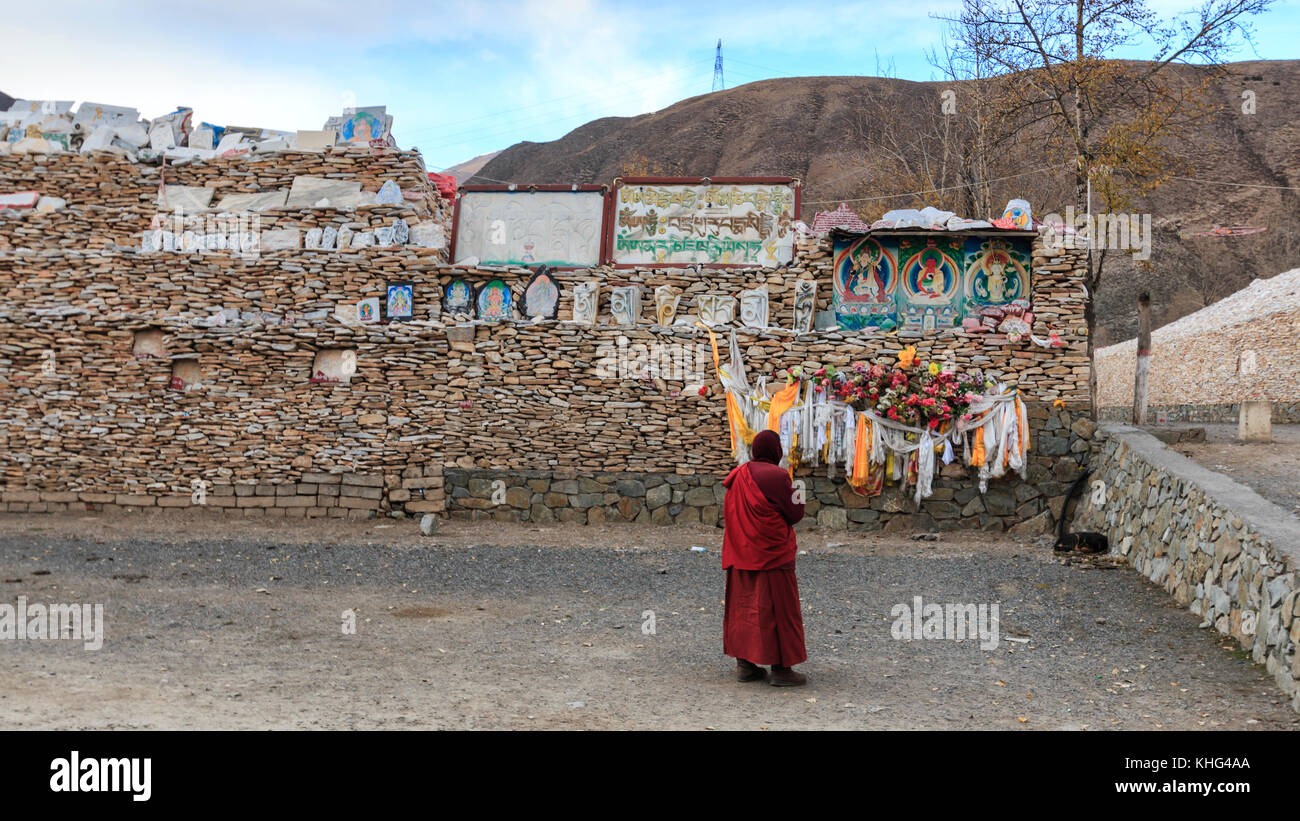 Yushu, Cina - 3 novembre 2017: Monaco tibetano che prega di fronte alle pietre mani al tempio mani (mani Shicheng) muro con mantra buddista Om mani Pad Foto Stock