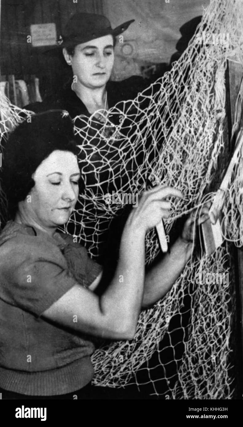 Questa fotografia storica mostra le donne impegnate nella realizzazione di reti mimetiche durante la seconda guerra mondiale, evidenziando il loro ruolo significativo nel sostenere lo sforzo bellico attraverso il lavoro domestico. Foto Stock