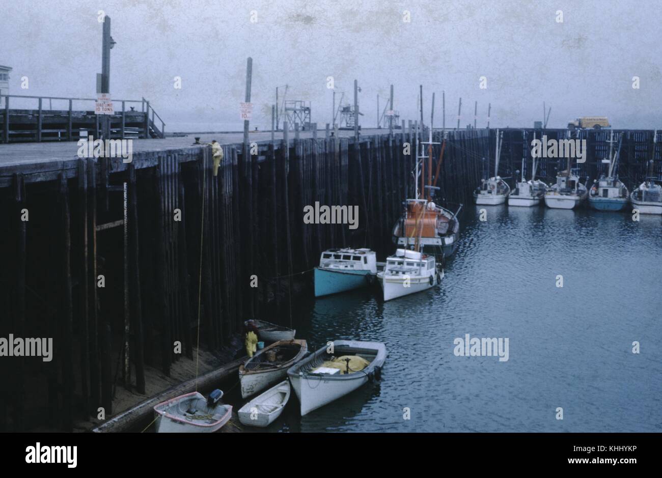 I pescatori con equipaggiamento giallo maledetto che scendono da una lunga scala da un molo a un gruppo di gommoni, in un giorno coperto, la fotografia originale della nuova Scozia mostra danni alla muffa, 1960. Foto Stock