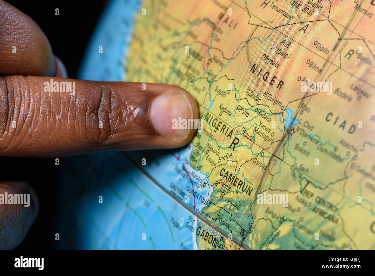 Dito di emigrante, indicando la sua patria Nigeria sulla mappa del mondo Foto Stock