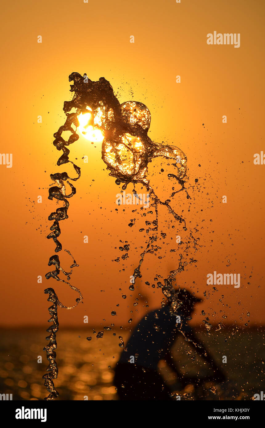 Acqua Splash isolato sul tramonto colori dello sfondo con la gente e gru silhouette. Foto Stock