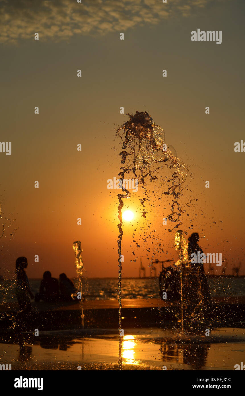 Acqua Splash isolato sul tramonto colori dello sfondo con la gente e gru silhouette. Foto Stock