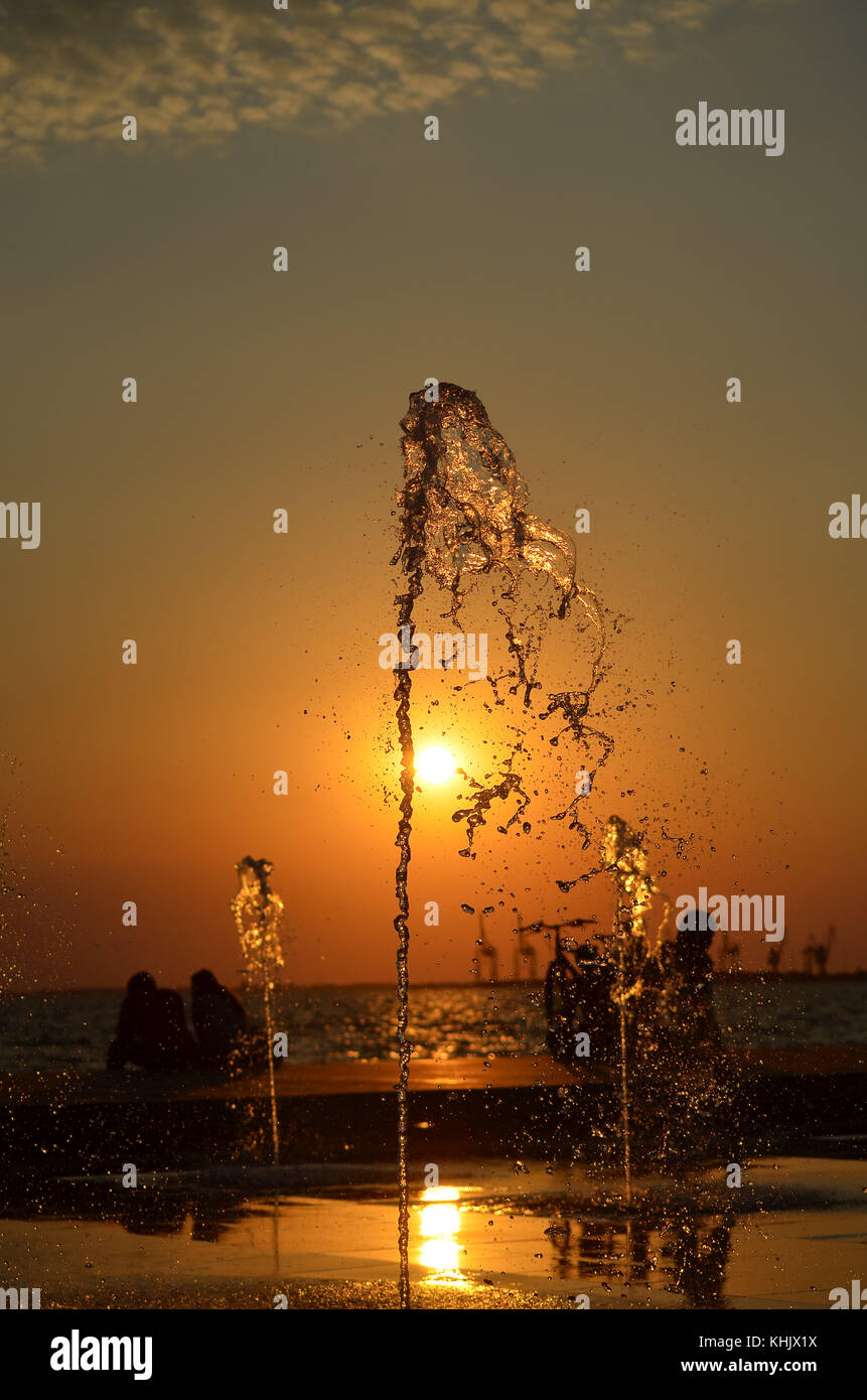 Acqua Splash isolato sul tramonto colori dello sfondo con la gente e gru silhouette. Foto Stock