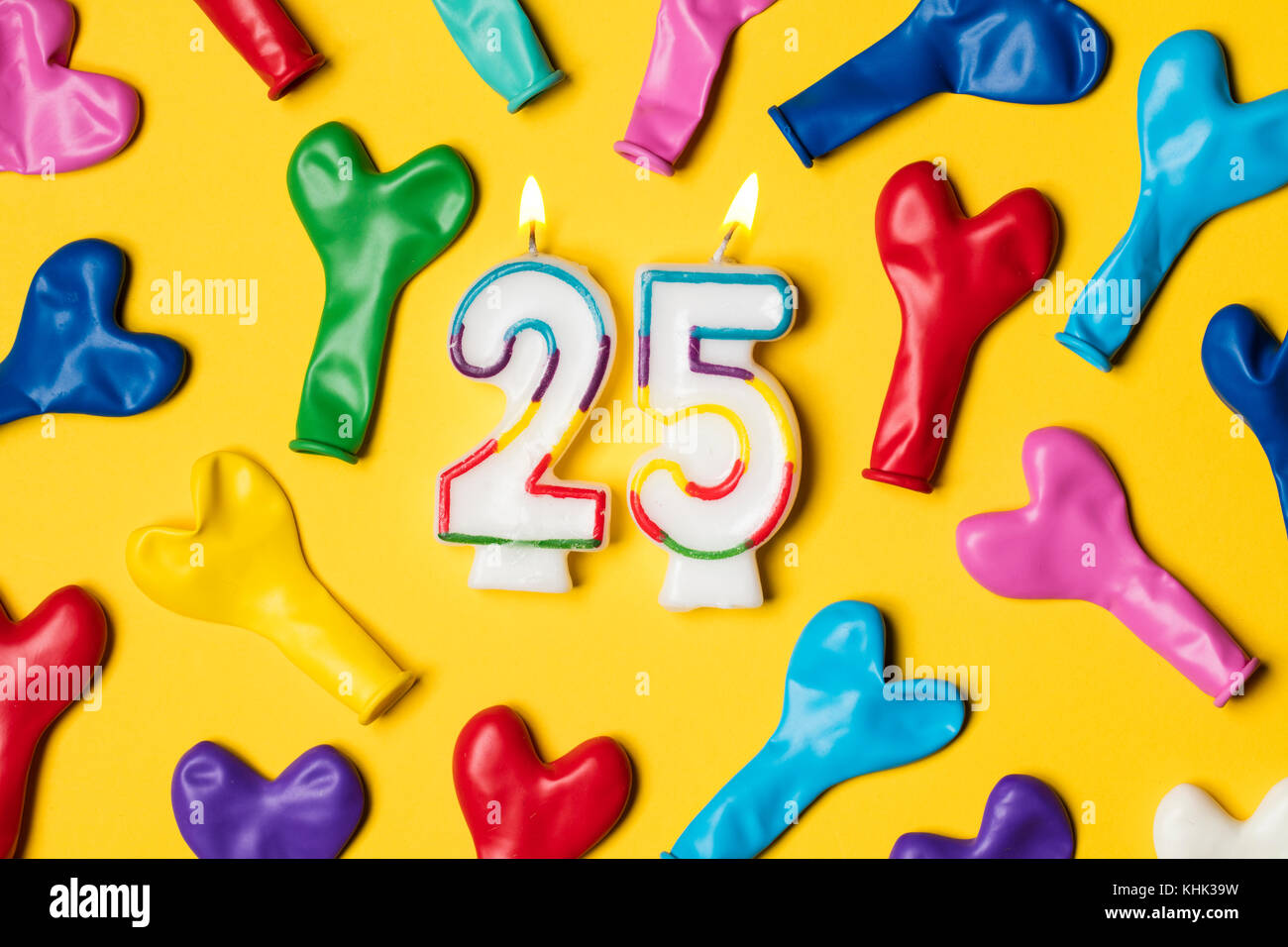 Numero 25 candela con palloncini di partito su un brillante sfondo giallo Foto Stock