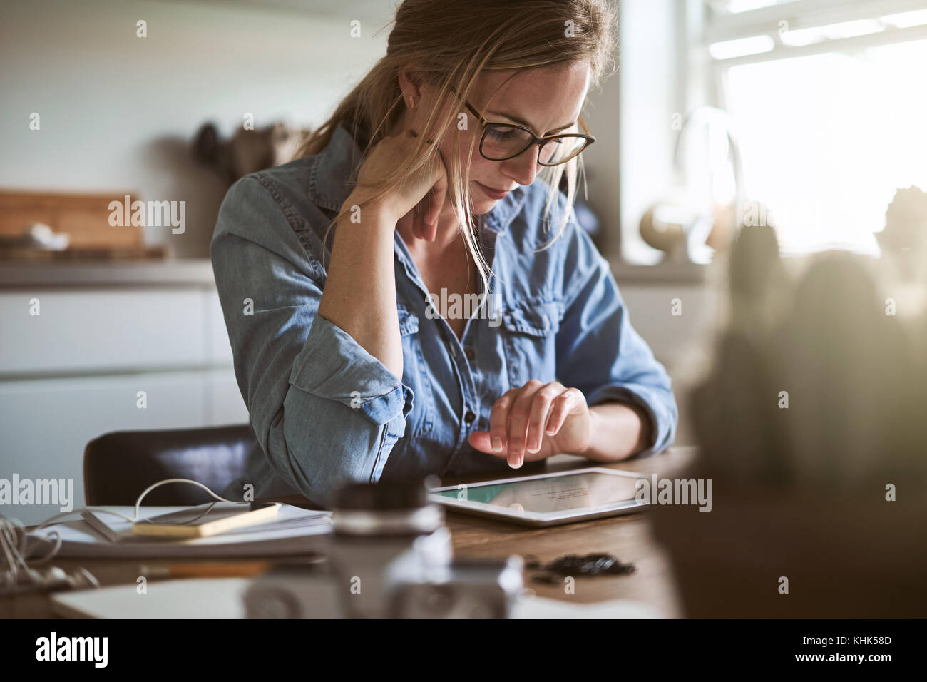 Focalizzato femmina giovane imprenditore lavorando alla sua piccola azienda con una tavoletta digitale mentre è seduto al suo tavolo da cucina a casa Foto Stock