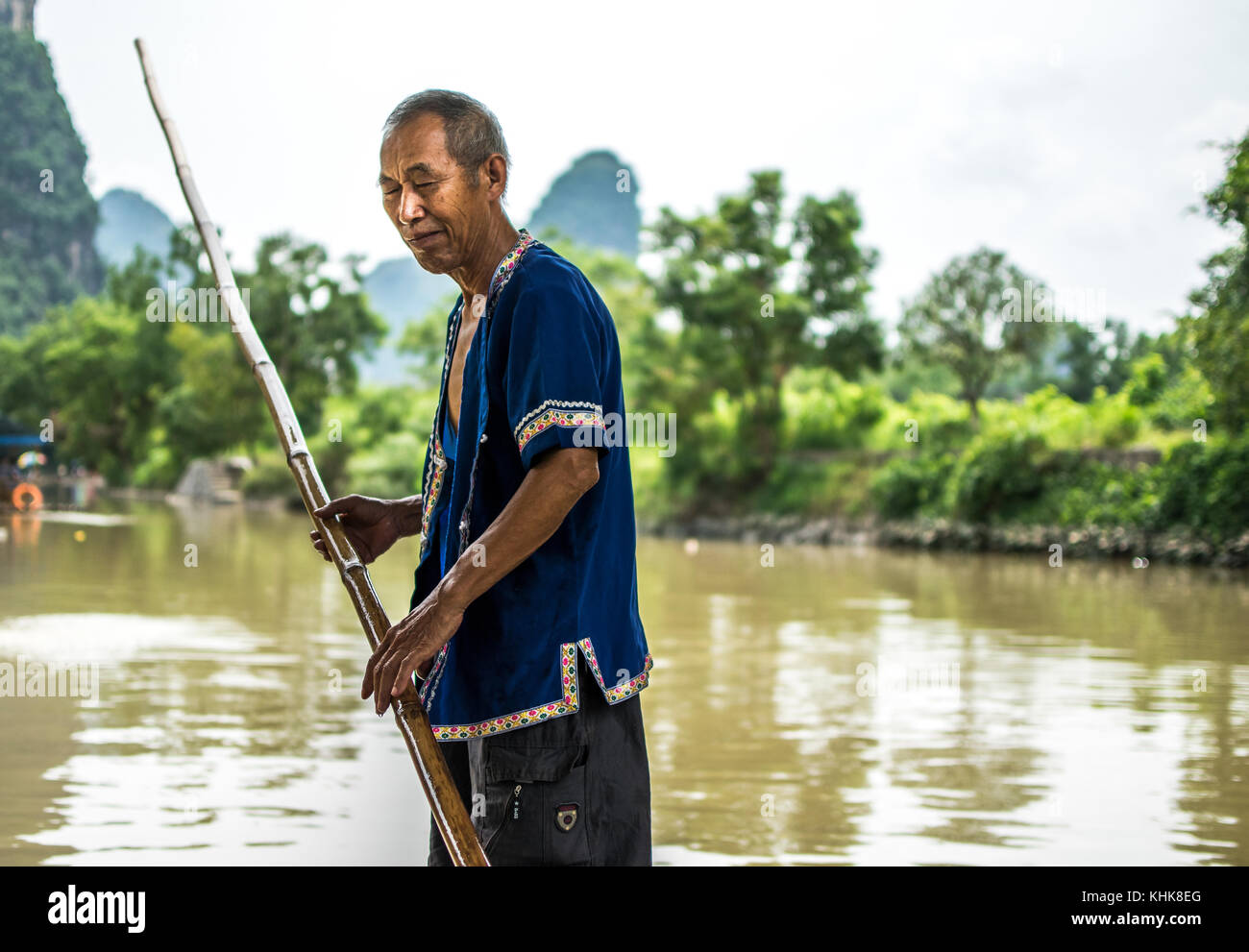 Il vecchio uomo cinese remare una barca con un bastone di bambù, il fiume li in Guilin, Cina Foto Stock