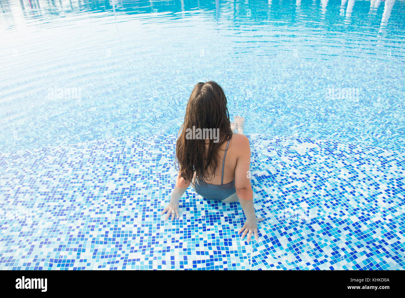 Vista posteriore di una donna in bikini sat in piscina Foto Stock