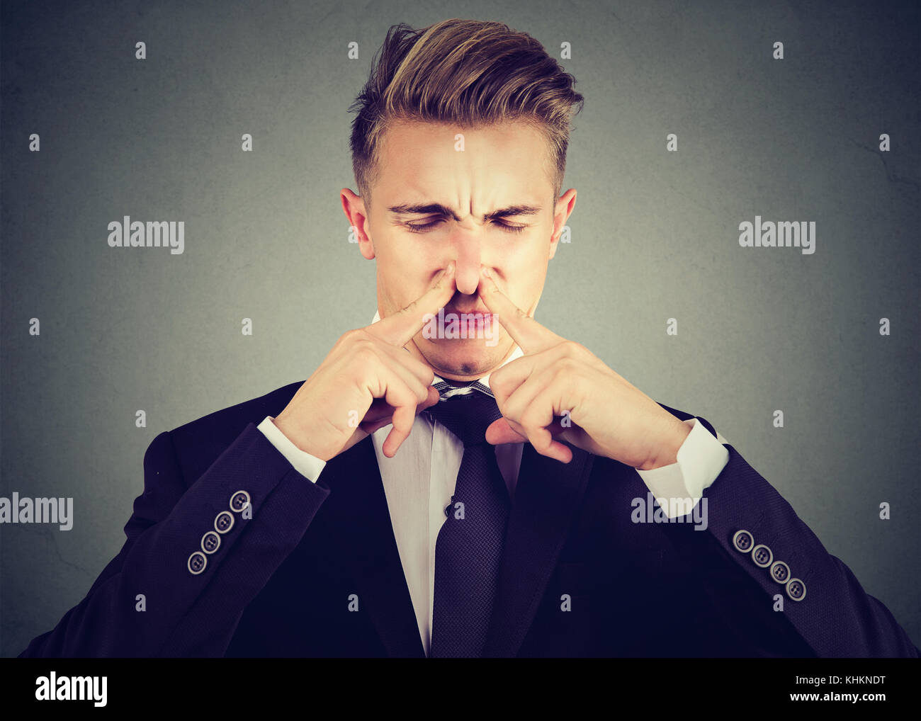 L'uomo pizzichi di naso con le dita guarda con disgusto puzza qualcosa di cattivo odore isolato su sfondo grigio. Foto Stock