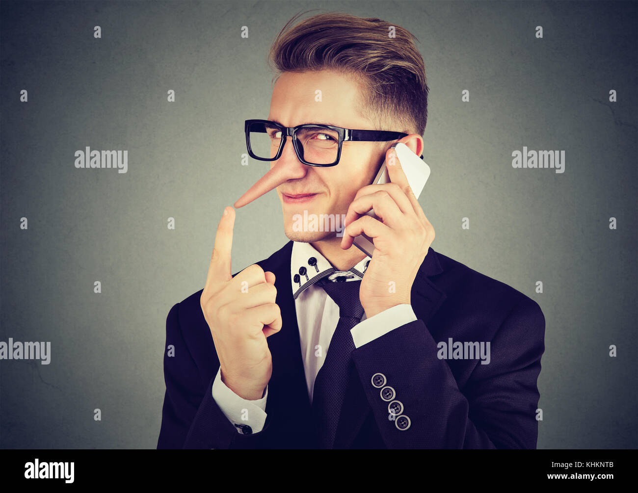 Giovane uomo di Sly con il naso lungo parlando al telefono cellulare isolata sul muro grigio Sfondo. bugiardo concetto emozione umana sentimenti Foto Stock