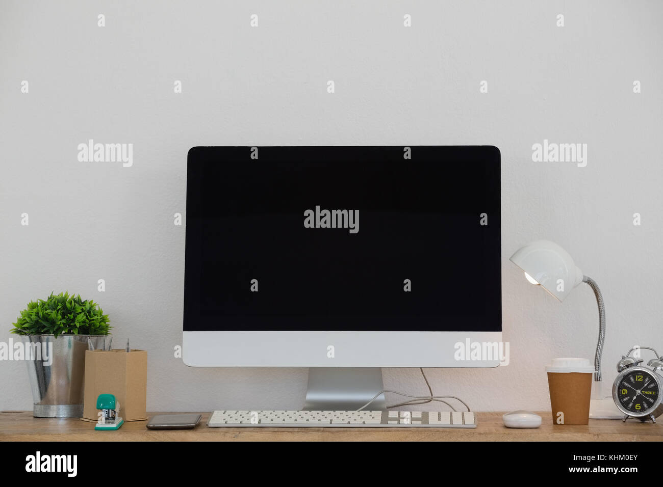 Lampada elettrica, il telefono cellulare e il pc desktop, bicchiere monouso, flora e articoli di cancelleria sulla tavola contro il muro bianco Foto Stock