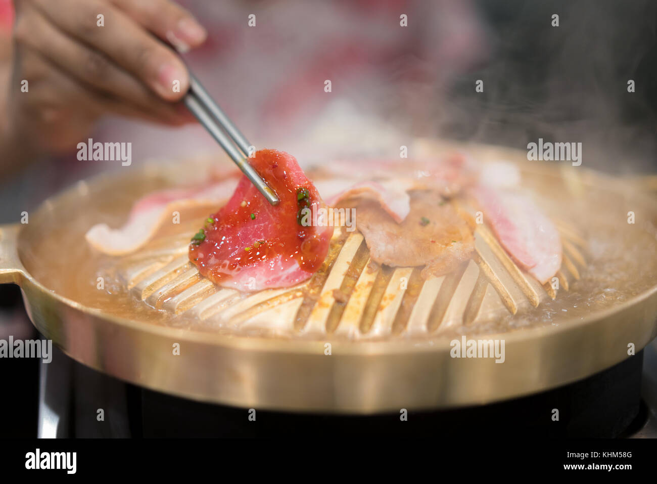Mano azienda chopstick con grigliate di carne di maiale coreano yakiniku alla griglia in stile giapponese. Foto Stock