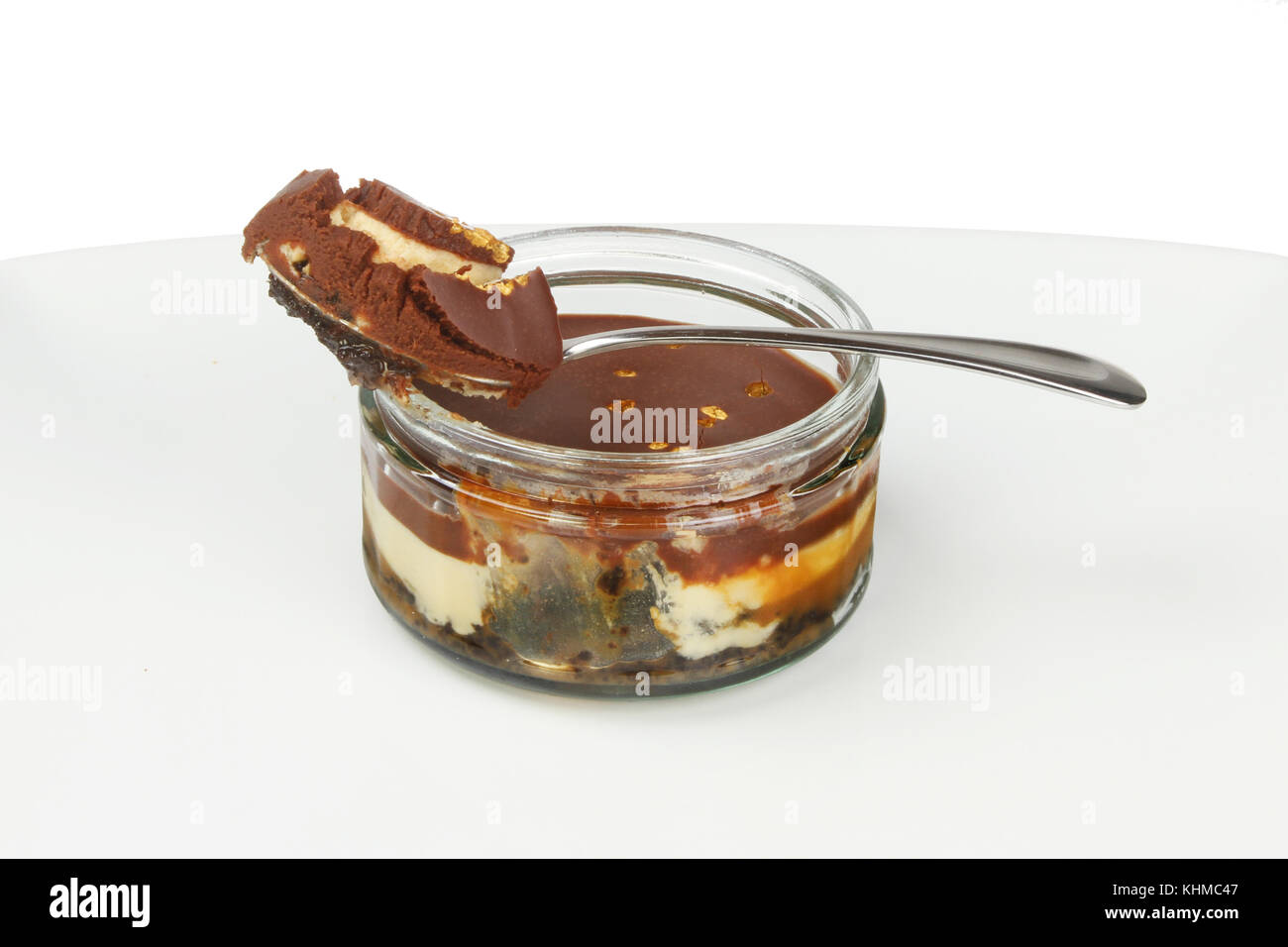 Luxury Chocolate cheesecake in un vetro ramekin con un cucchiaio su una piastra contro uno sfondo bianco Foto Stock
