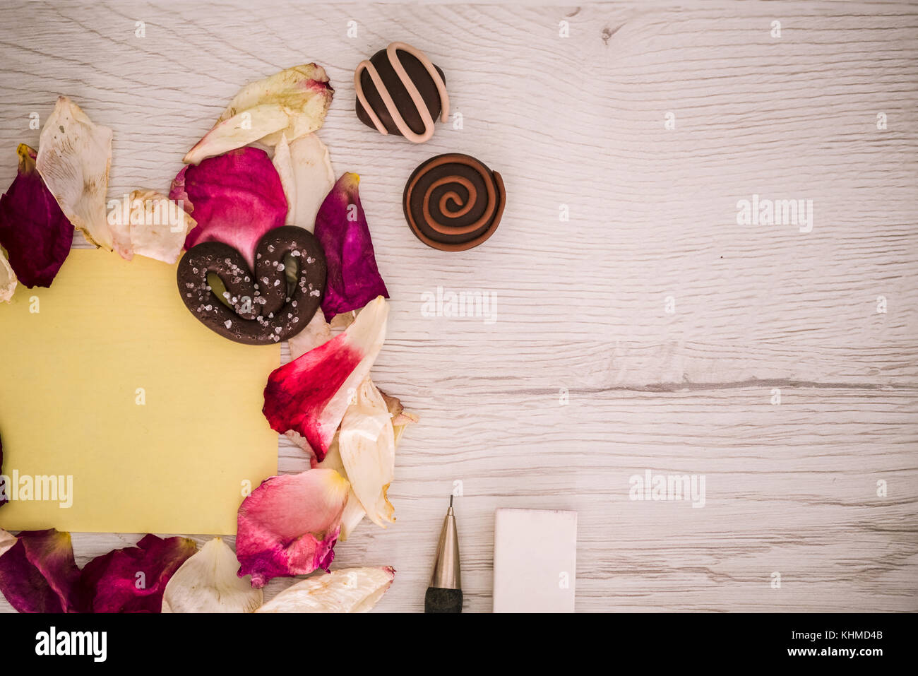 Petali, cioccolato, matita e una gomma su sfondo bianco Foto Stock