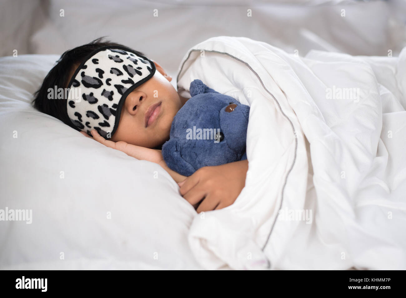 Bambino addormentato sul letto con Teddy bear cuscino bianco e fogli di indossare la maschera di sospensione.boy addormentarsi in mattinata.concetto del sonno Foto Stock