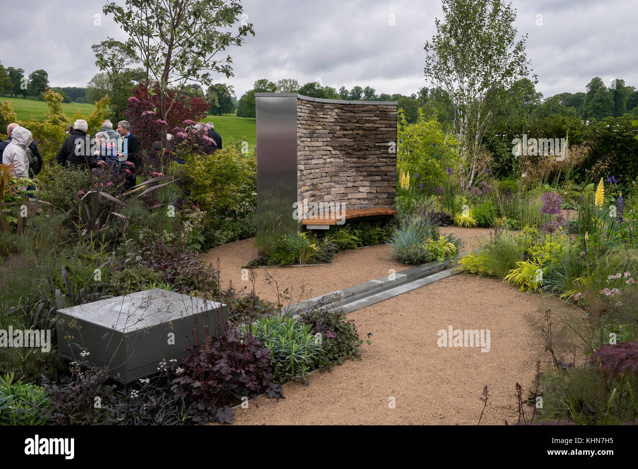 Gli ospiti passano tranquilla e appartata area con posti a sedere e piante in un giardino mostra in prima RHS Chatsworth Flower Show, la Chatsworth House, Derbyshire, Inghilterra, Regno Unito. Foto Stock
