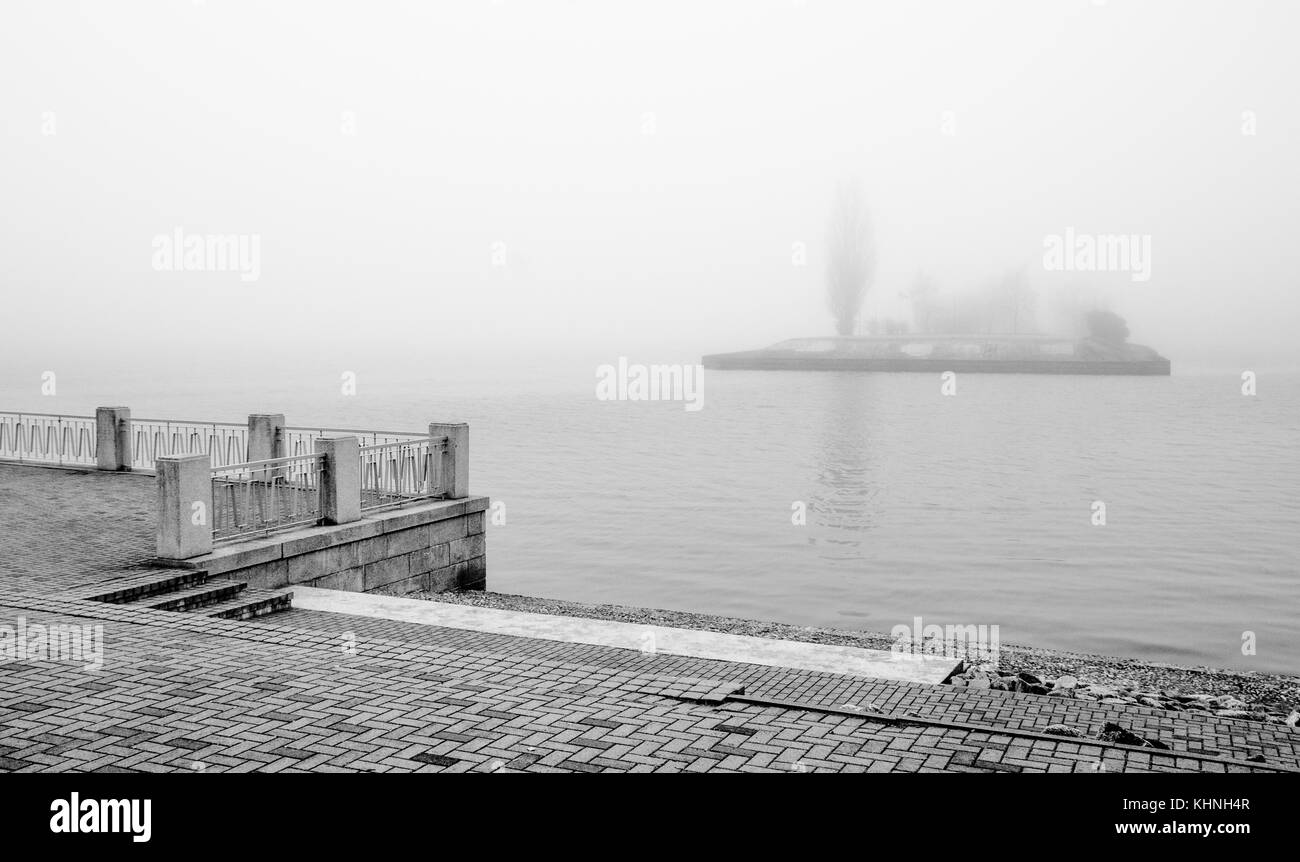 Un bianco e nero foto di una banca del fiume Daugava nel centro di riga in una nebbiosa mattina con una lontana isola di scomparire nella nebbia. Foto Stock