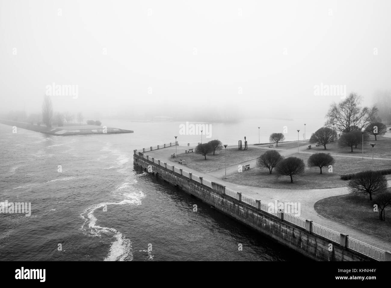 Un bianco e nero foto di un parco sulla riva del fiume Daugava nel centro di riga in una nebbiosa mattina con un lontano in riva al fiume scomparendo nella nebbia. Foto Stock