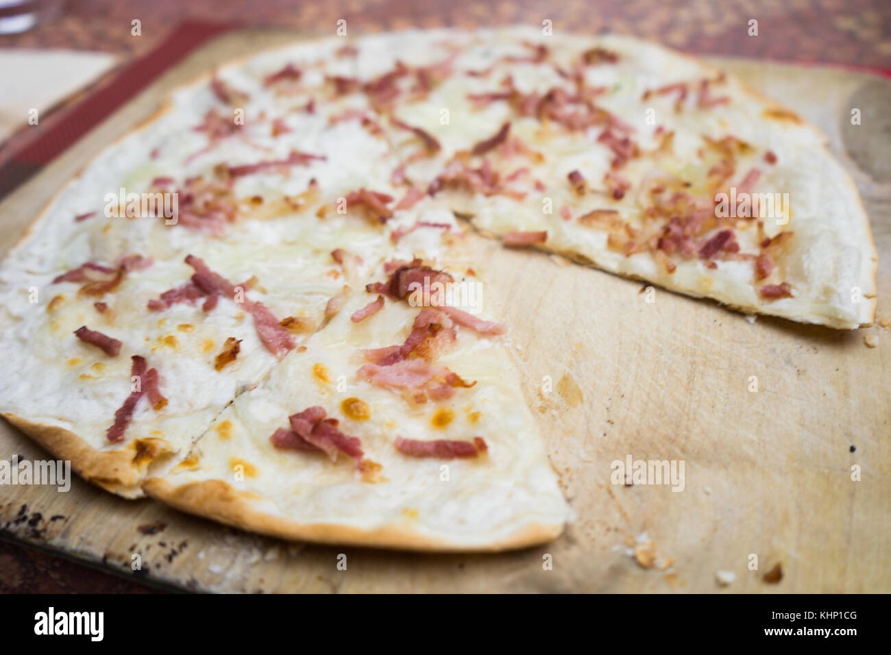 Tradizionale alsaziano Flammkuchen pizza flatbread su piatto di legno con una fetta mancante Foto Stock