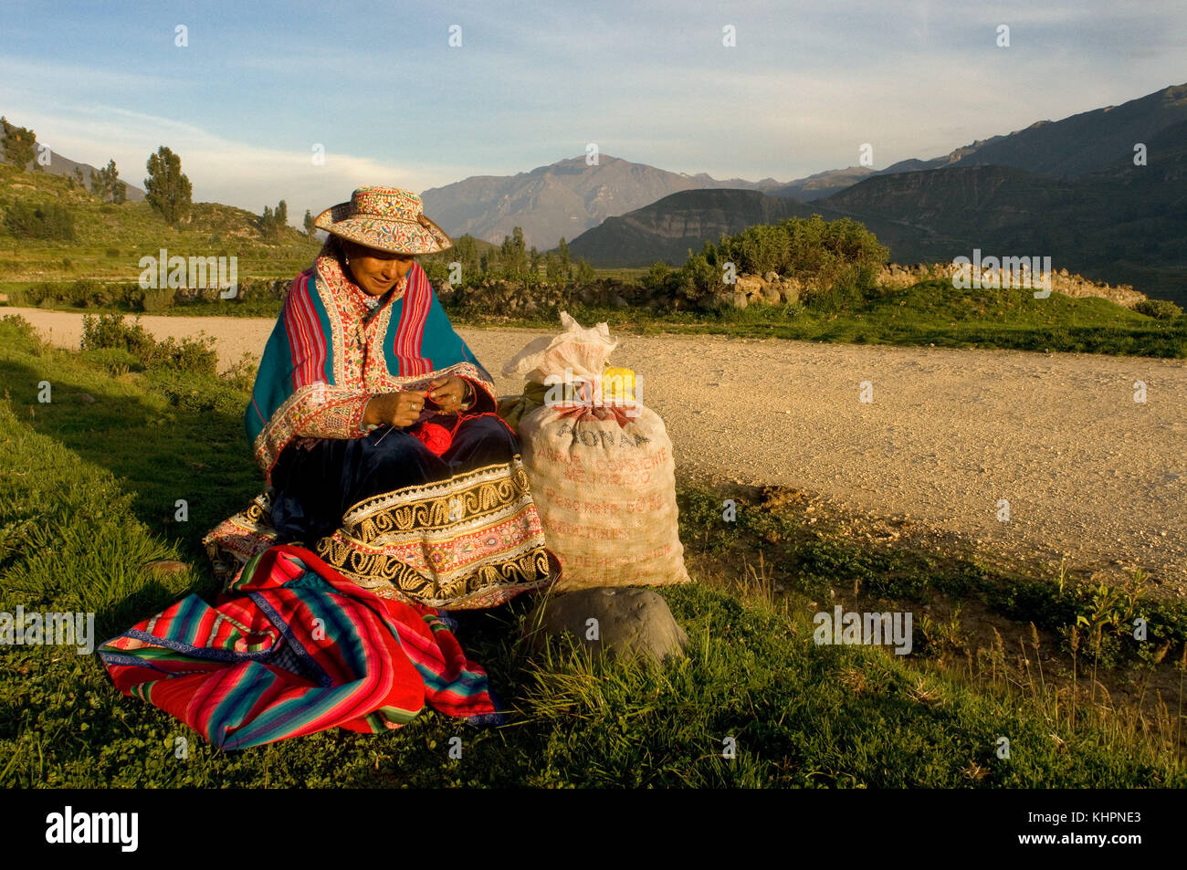 Una donna attende il trasporto per portare i sacchi di patate che ha raccolto vicino a Chivay. Zona della Valle di Colca, Chivay, Perù Foto Stock