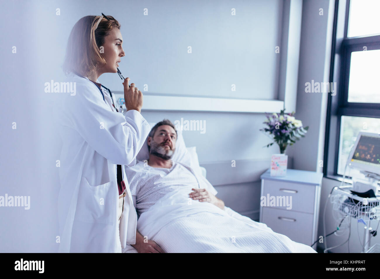 Medico nella stanza di ospedale guardando il dispositivo di monitoraggio paziente con uomo malato giacente in letto. Medico prendendo la decisione per il trattamento su ricoverato l'uomo. Foto Stock