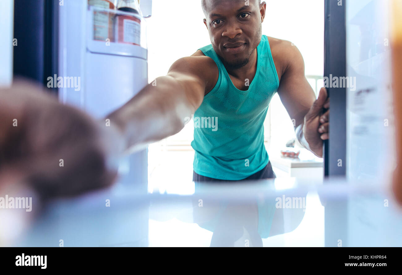 Uomo che mette qualcosa nel frigo a casa. gli appassionati di fitness utilizzano un frigorifero dopo un allenamento. Foto Stock
