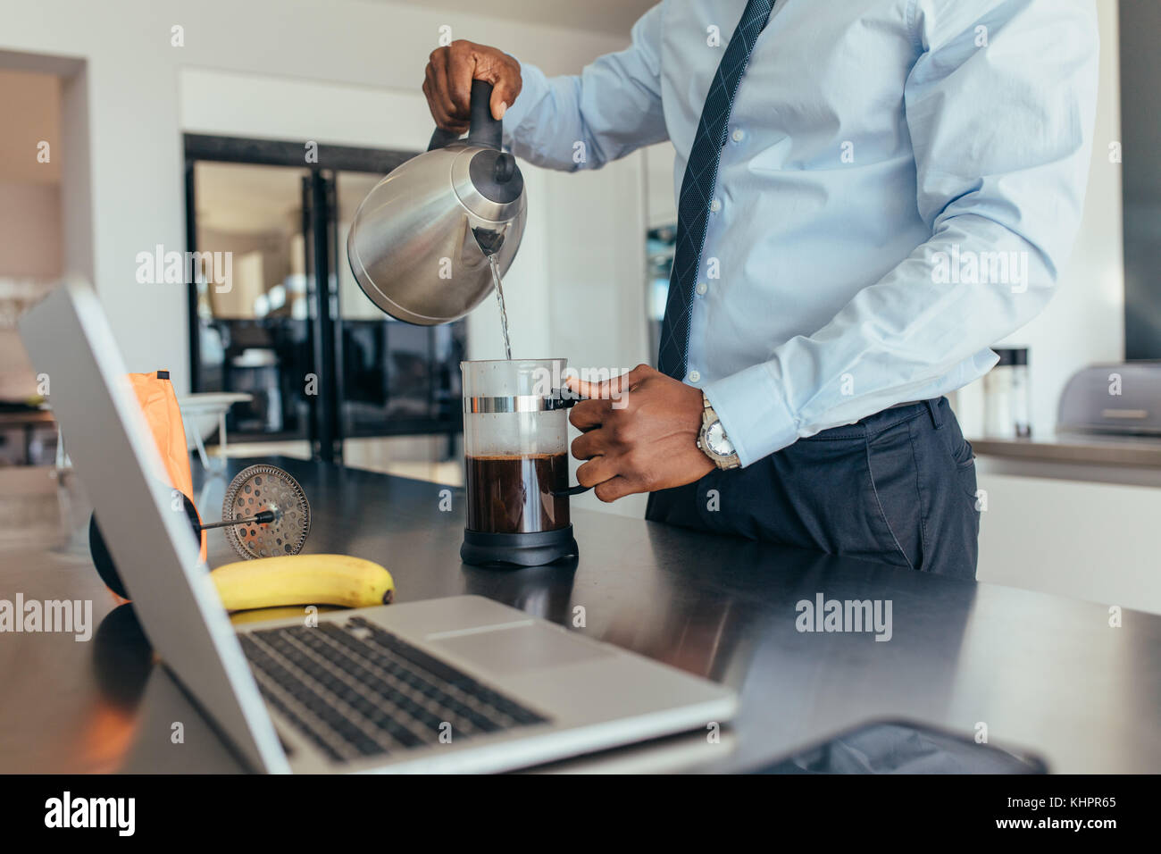 Uomo che versa acqua calda nella macchina per il caffè. uomo d'affari che prepara il caffè al tavolo della colazione con un computer portatile accanto. Foto Stock