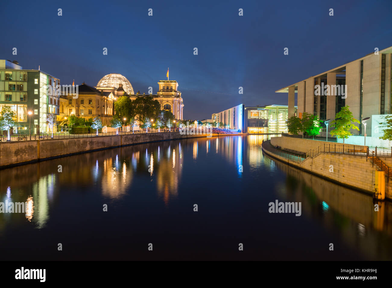 Berlino, Germania - 26 agosto 2017; persone sedute sul terrapieno in distanza sotto illuminato riechstag dome, edifici circostanti e riflessa colo Foto Stock