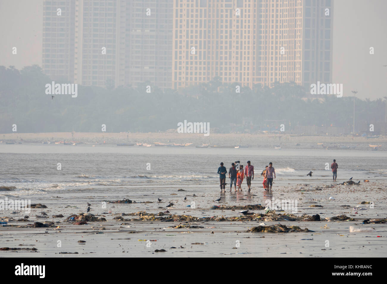 La gente camminare tra immondizia di plastica e altre acque reflue a bassa marea sulla spiaggia versova, Mumbai Foto Stock