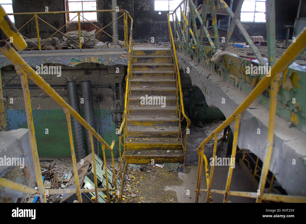 Scala con ringhiera gialla in una rovina industrial interior. dimenticato vecchia fabbrica. Foto Stock