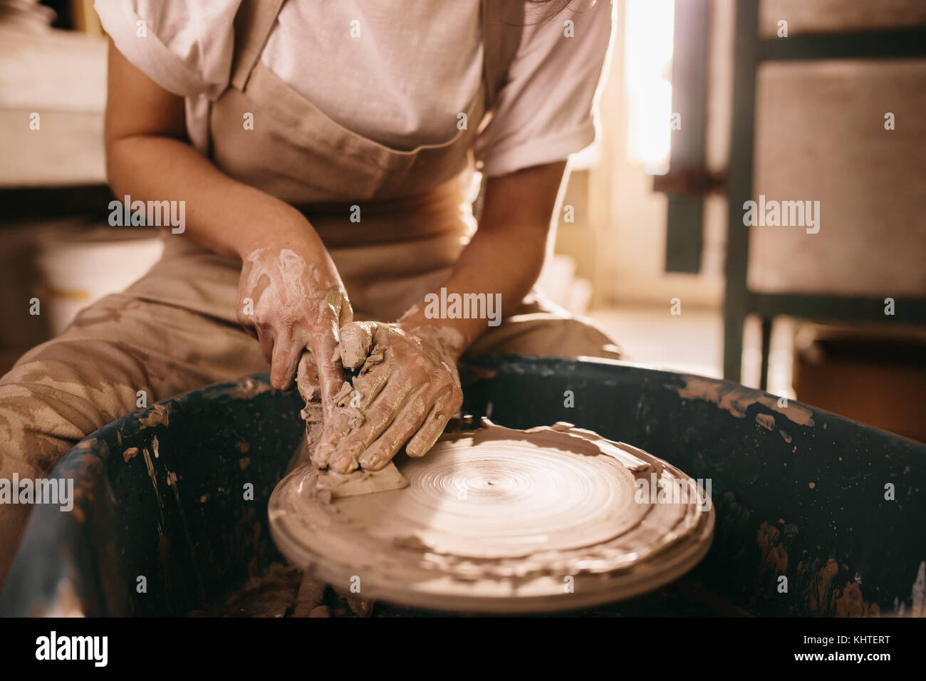 Donna di argilla di appiattimento sulla ruota di ceramiche in officina. Craftswoman lavorando su argilla con utensile di schiacciamento sulla ruota di ceramiche. Foto Stock