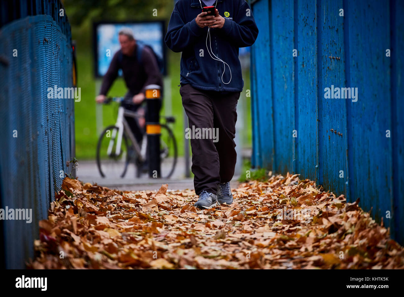 Una persona in un Morrisons uniforme a piedi lungo un sentiero pieno di caduto foglie di autunno in Winsford, Cheshire. Foto Stock