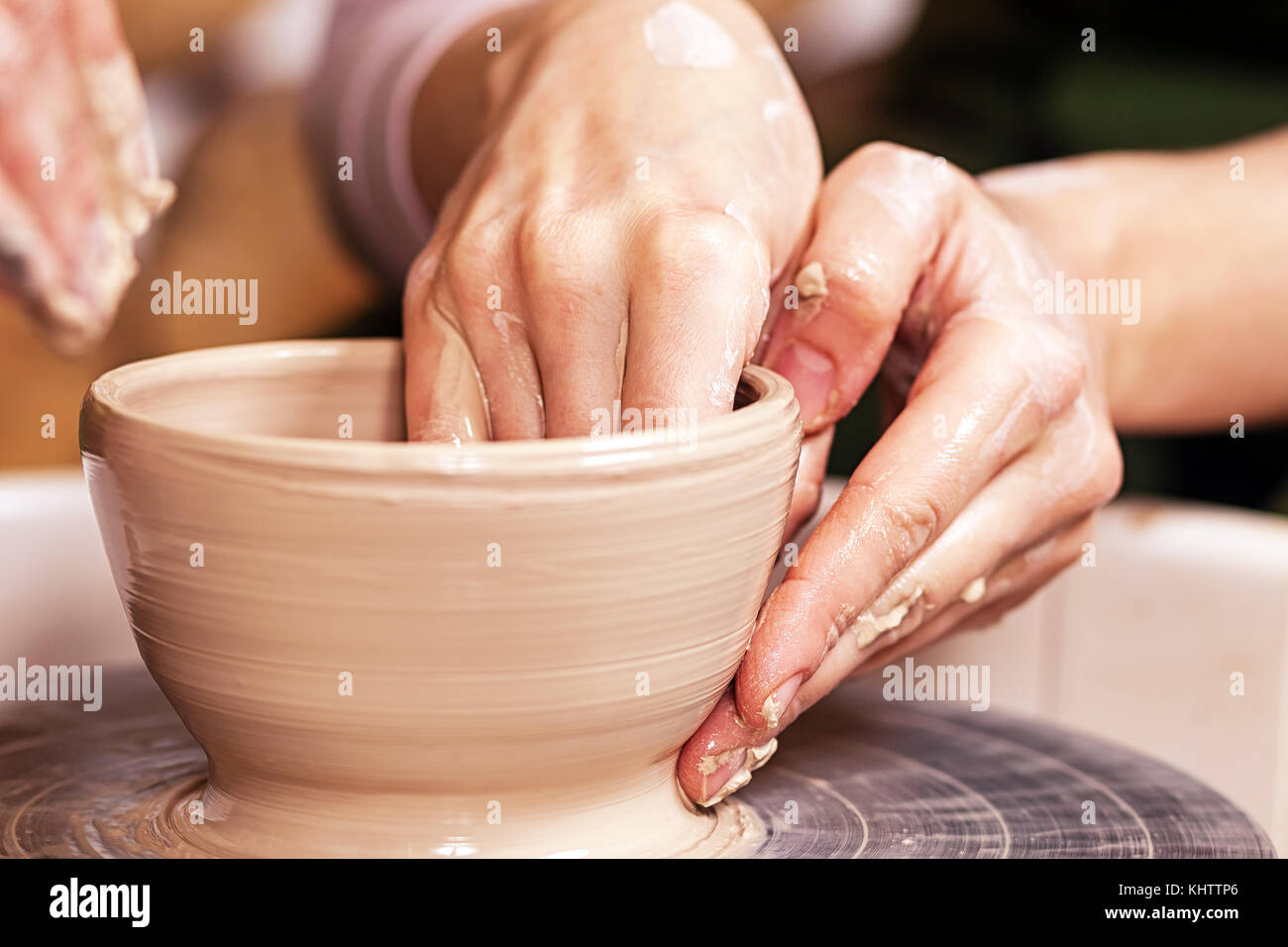 Close-up di una giovane donna potter scolpire su un tornio del vasaio un vaso fatto di argilla marrone, rende un bordo liscio alla ciotola in officina creativa, si Foto Stock