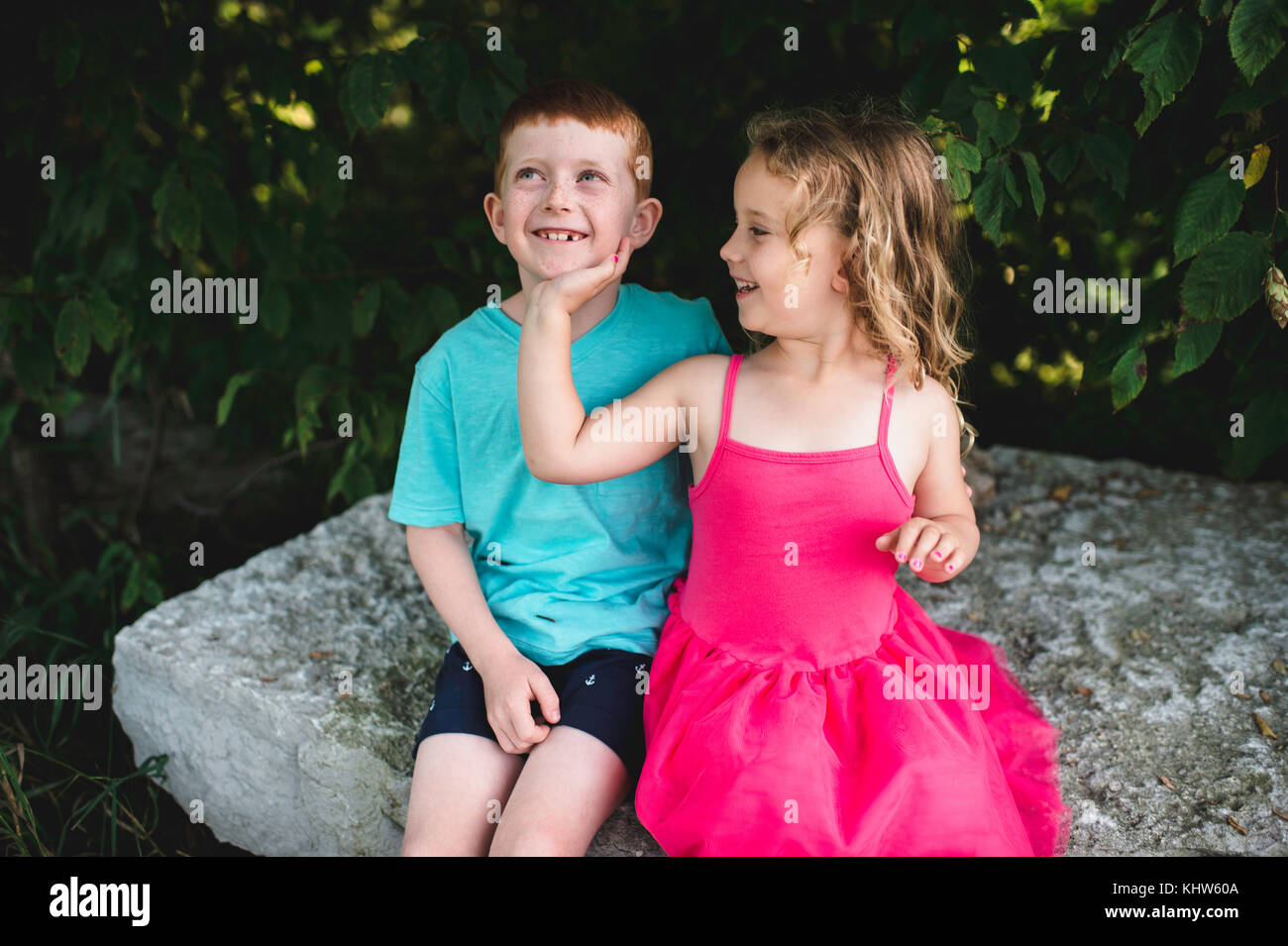 Ragazza con mano sul fratello del mento, seduto su roccia Foto Stock