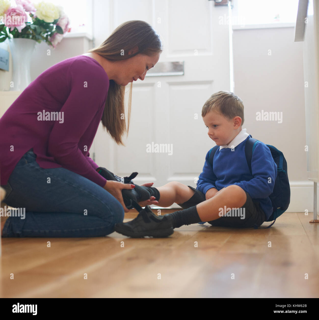 Donna mettendo sul figlio della scuola di scarpa in corridoio Foto Stock