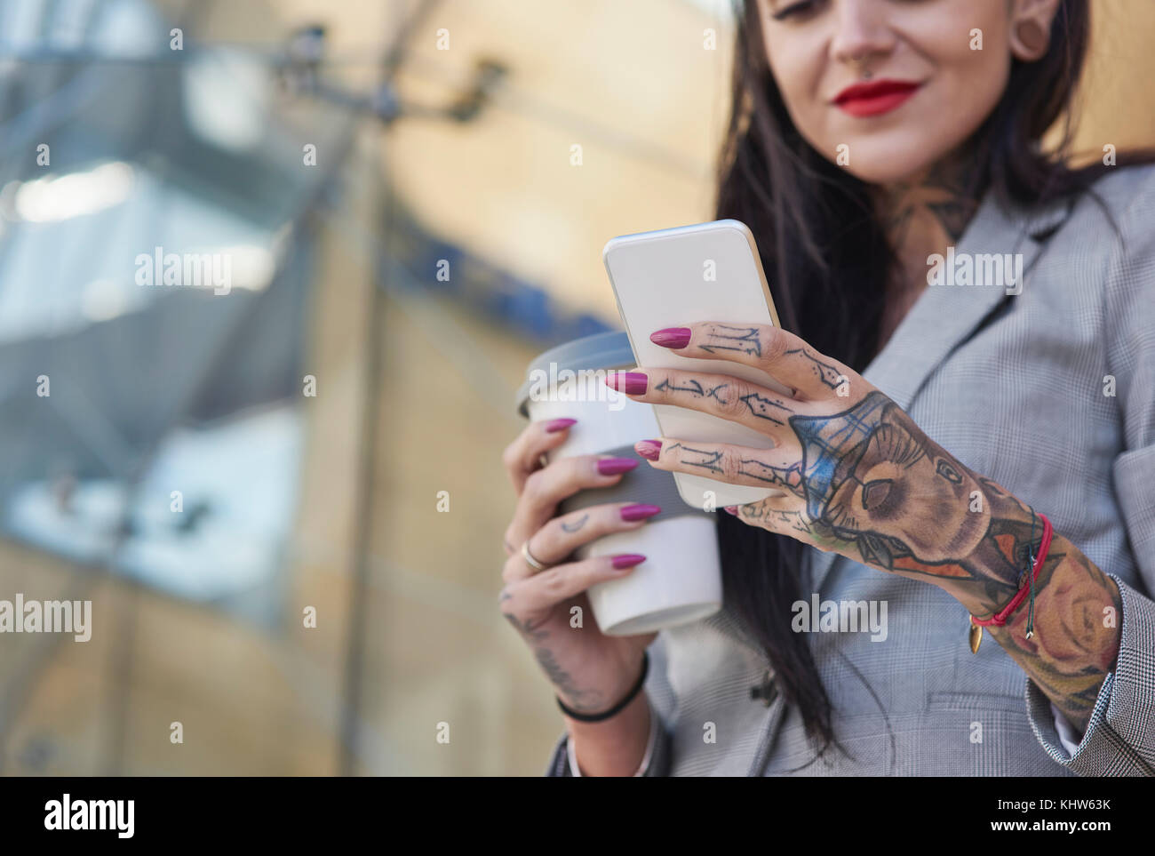 Imprenditrice all'aperto, tenendo tazza da caffè, utilizza lo smartphone, tatuaggi sulle mani, metà sezione Foto Stock