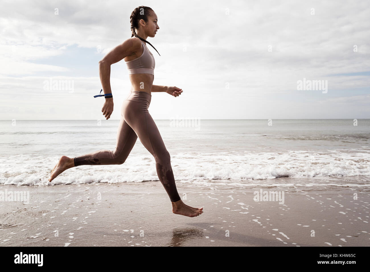 Vista laterale del giovane femmina runner correre a piedi nudi lungo il bordo d'acqua a beach Foto Stock