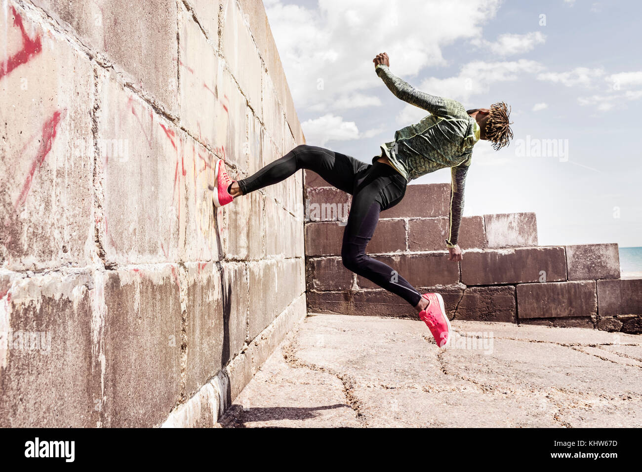 Giovane uomo, free running, esterni in esecuzione su parte della parete Foto Stock