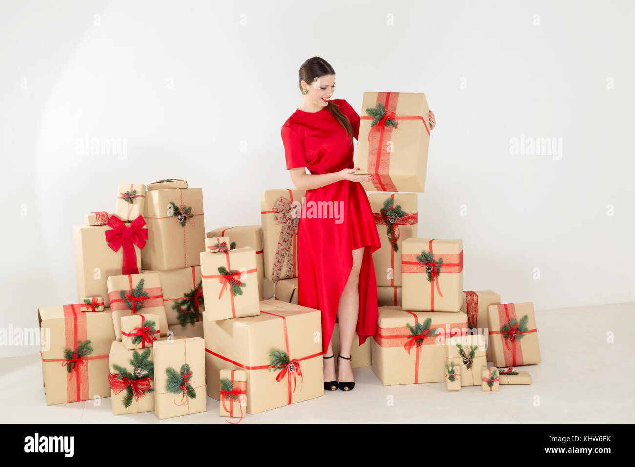 Giovane donna in abito rosso per impilata regali di Natale tenendo il pacco di Natale Foto Stock