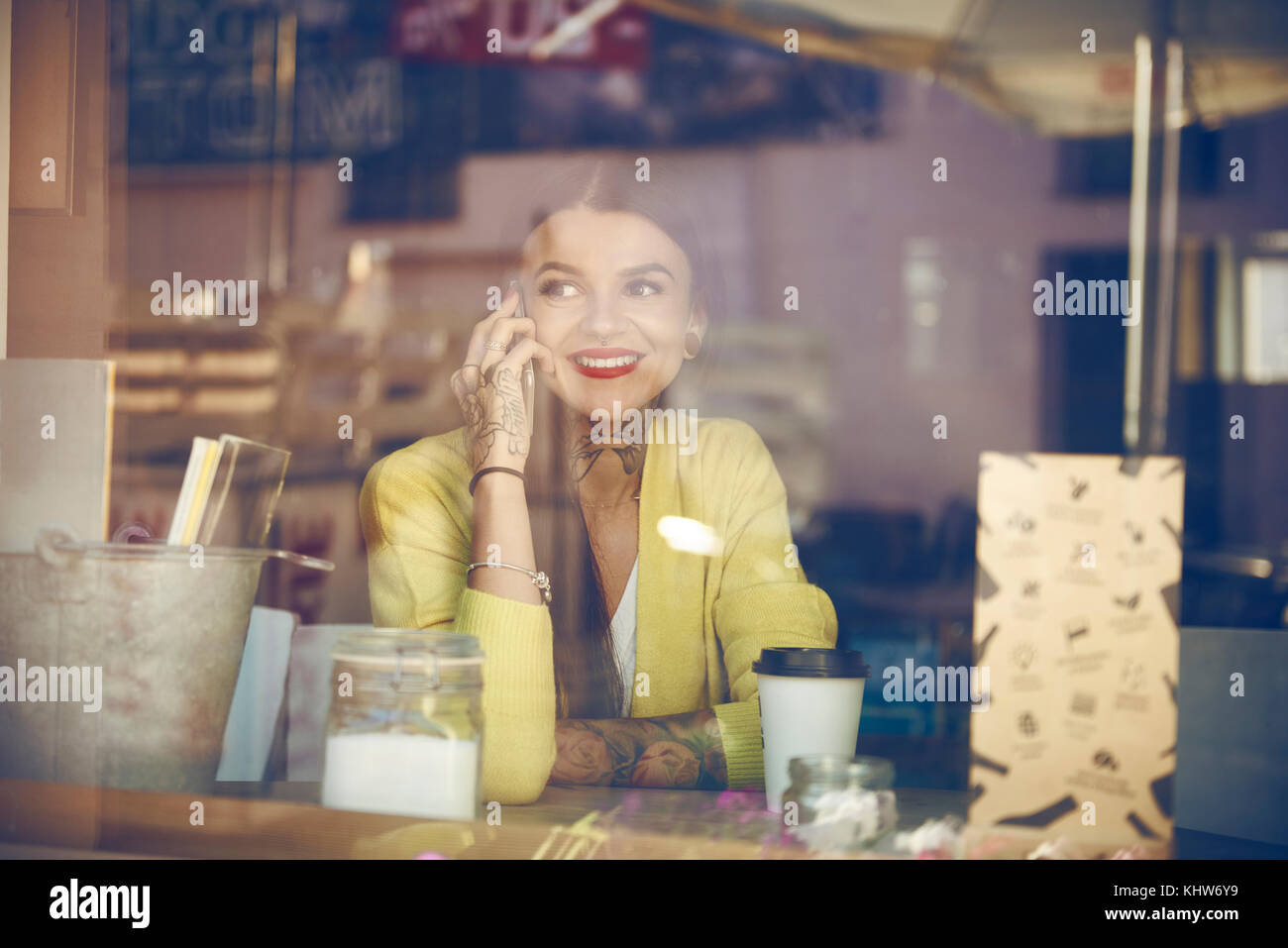 Giovane donna seduta al cafe, utilizza lo smartphone, tatuaggi sul lato vista attraverso la finestra cafe Foto Stock