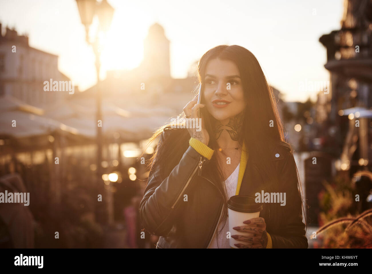 Giovane donna passeggiate all'aperto, tenendo tazza da caffè, utilizza lo smartphone, tatuaggi sulle mani e collo Foto Stock