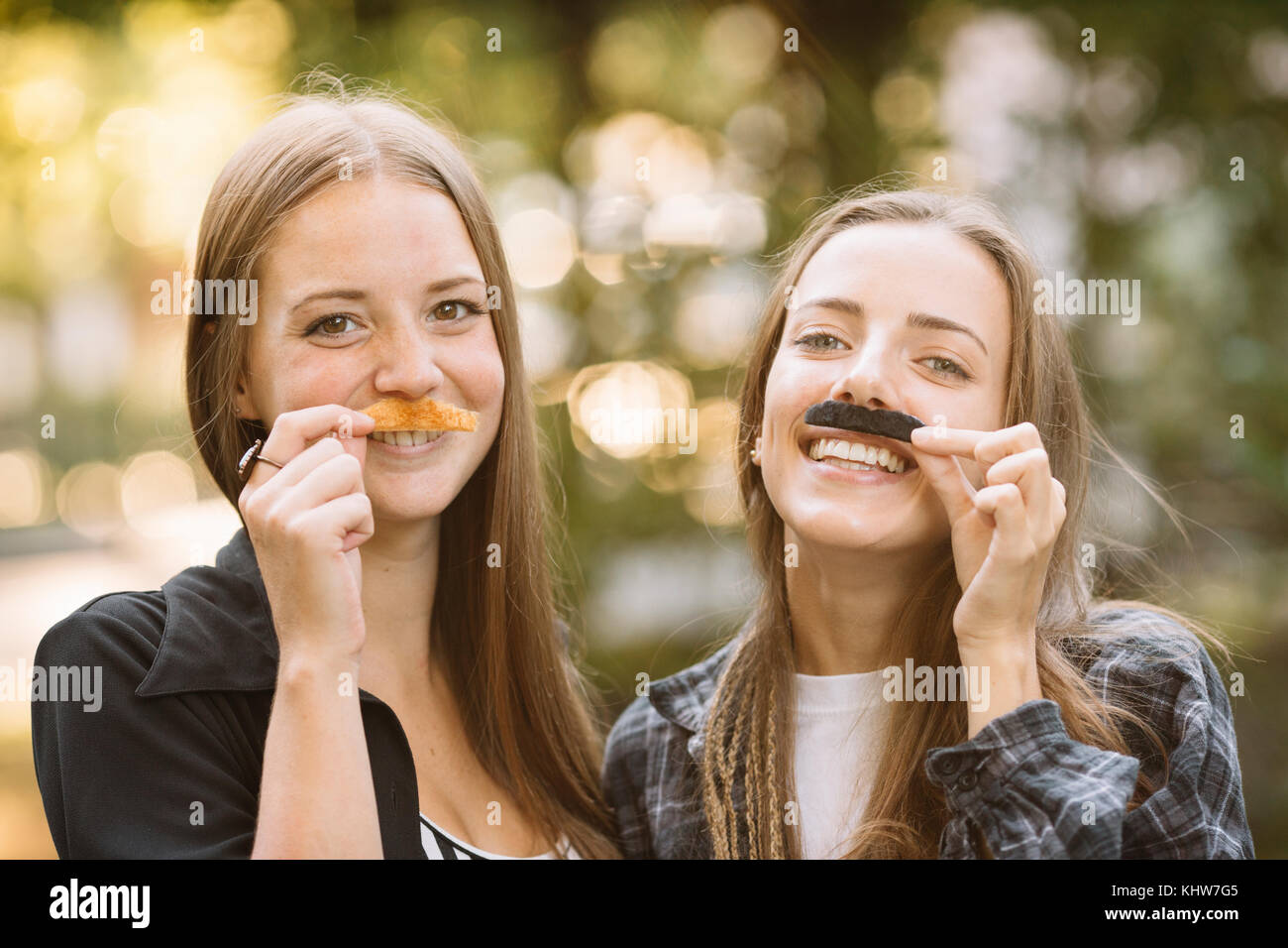 Ritratto di due giovani amici di sesso femminile azienda falso di baffi a loro volto in posizione di parcheggio Foto Stock