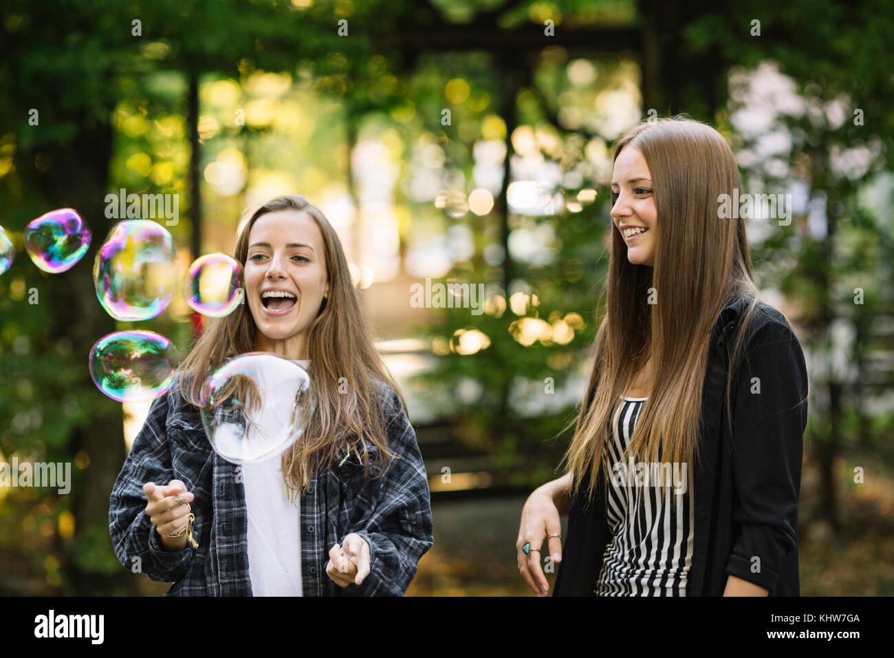 Due giovani amici di sesso femminile scoppiare bolle flottante in posizione di parcheggio Foto Stock
