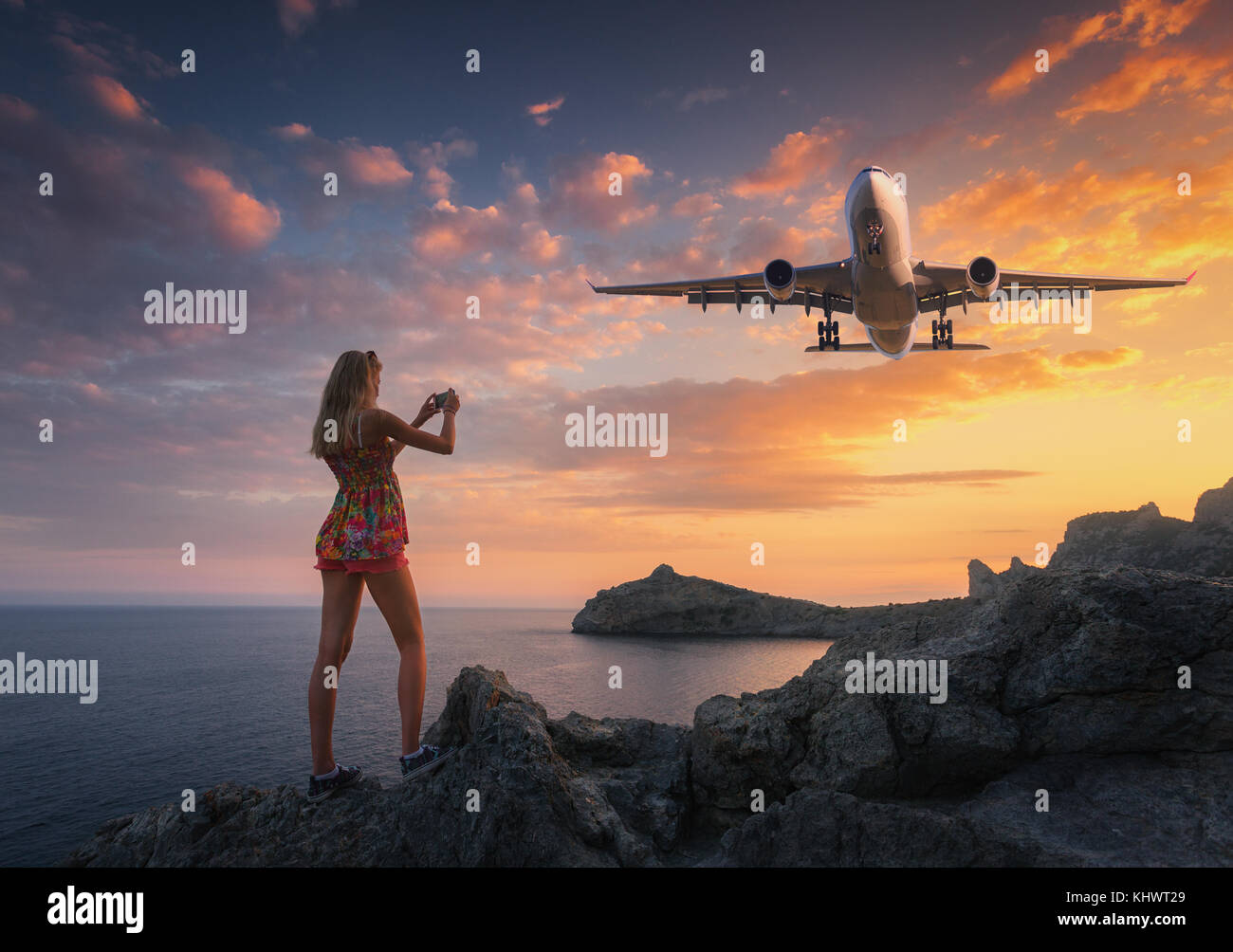 Bella donna rende la foto di aerei di atterraggio al tramonto. Paesaggio estivo con la ragazza in piedi sulle rocce e Battenti aereo passeggeri contro colo Foto Stock