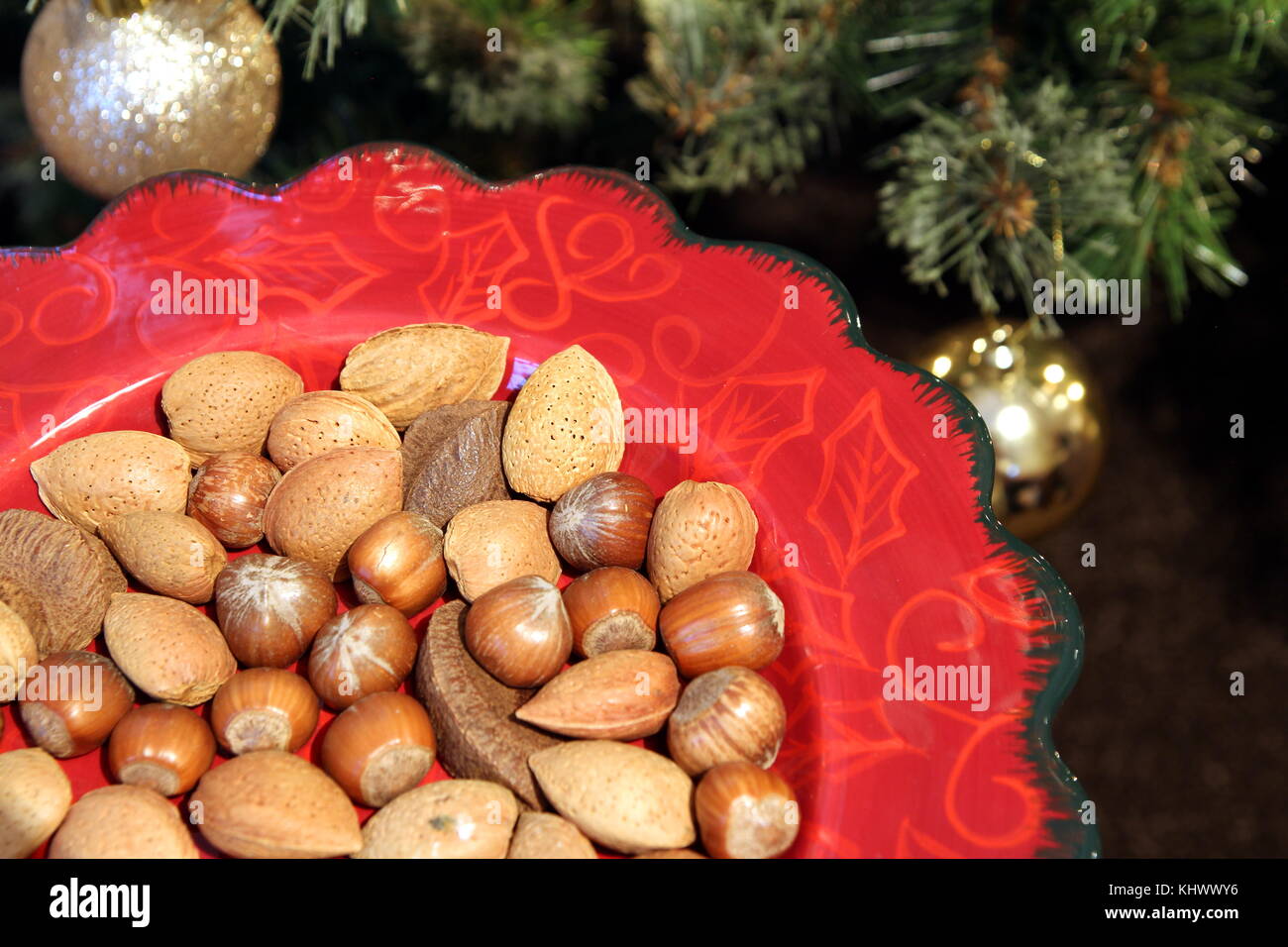 Bella rossa piastra di natale con la festa tradizionale di mandorle, nocciole e noci del Brasile, con un albero di natale in background Foto Stock