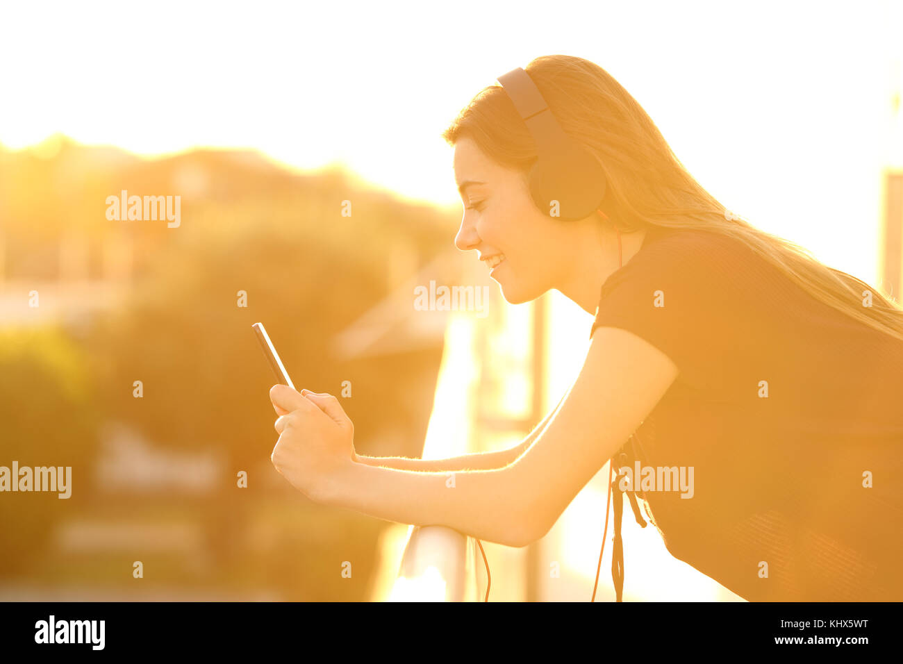 Vista laterale verticale di una ragazza utilizzando un telefono intelligente in un balcone al tramonto Foto Stock