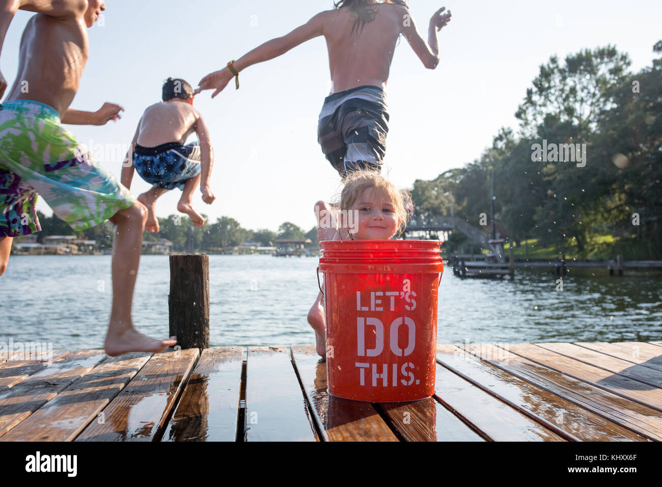 Ragazza giovane di nascondersi dietro la benna sul molo, bambini saltando nel lago Foto Stock
