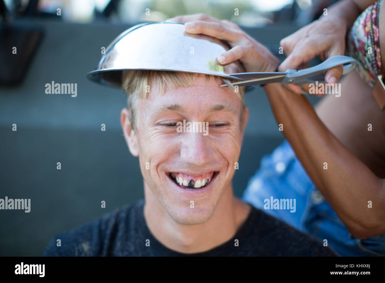 Taglio donna giovane di capelli usando ciotola, uomo di denti oscurati Foto Stock